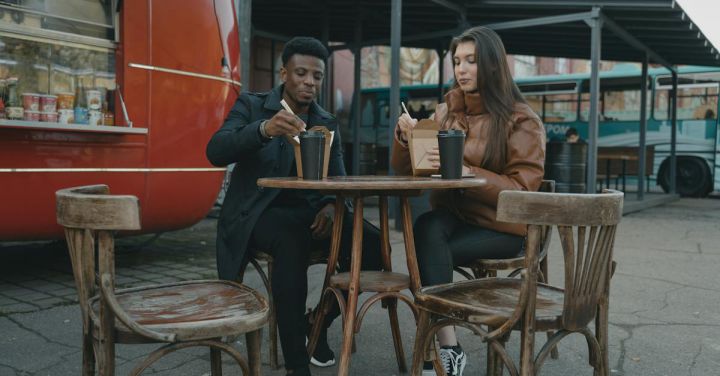 Dining Out - A Man in a Black Coat and a Woman in a Brown Jacket Dining Outdoors