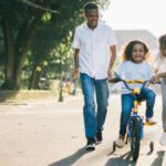 Family Fun - Man Standing Beside His Wife Teaching Their Child How to Ride Bicycle