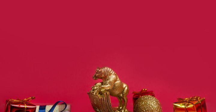 Event Calendar - Symbolic golden bull figurine with wrapped New Year gifts and bauble placed on shiny table with coins stack and rolled dollar banknotes against red background